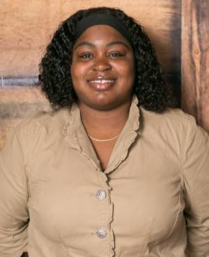 A woman with curly hair wearing a tan shirt.