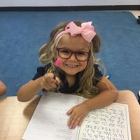 A little girl with glasses and bow tie sitting at a desk.